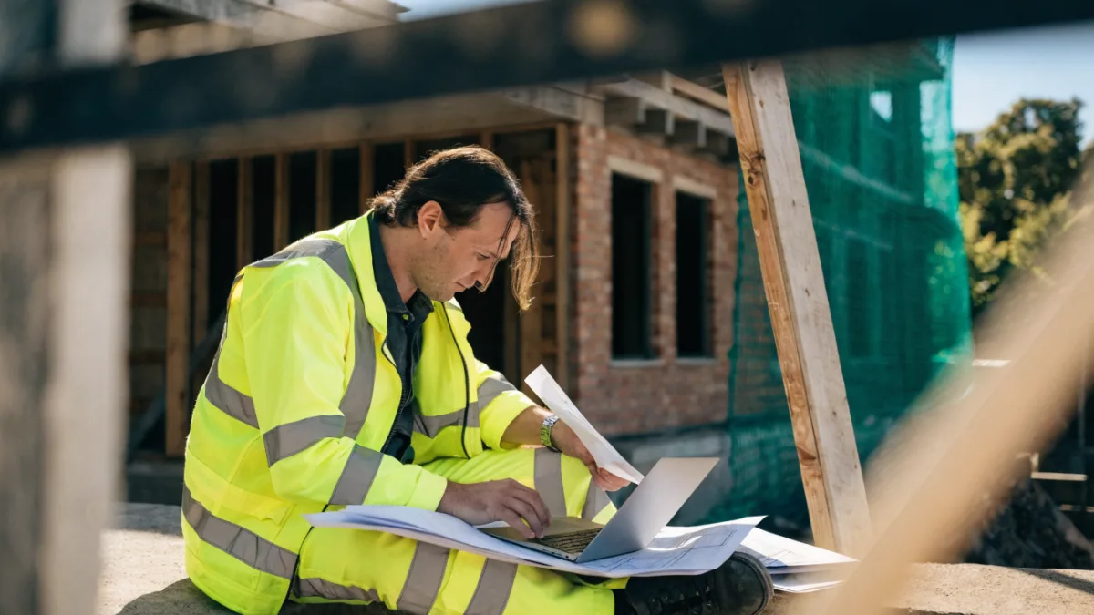 Construction business owner reviewing plans and a laptop on site