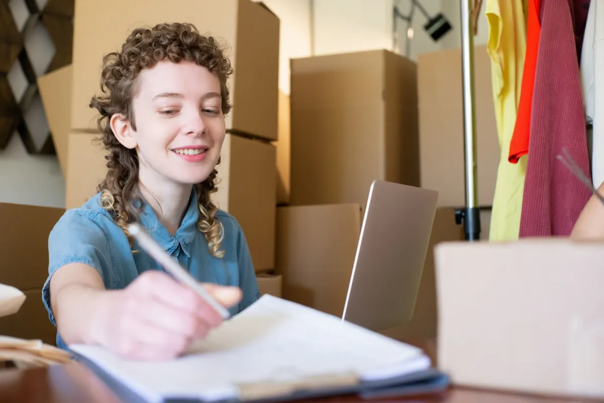 Small-business owner writing at a desk surrounded by stock boxes