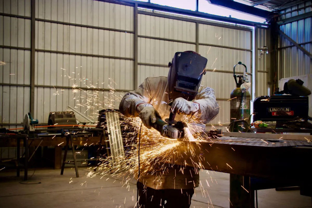 Welder in a metal fabrication workshop grinding steel, sparks flying