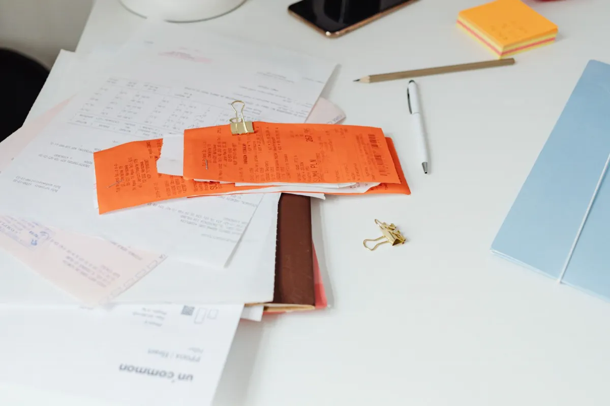 Unpaid invoices and receipts piled on a desk beside a pen and phone