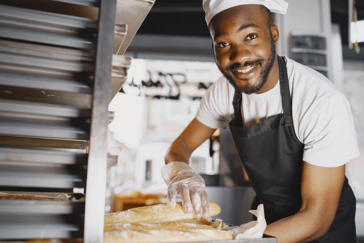 Baker holding a tray of fresh baguettes in a bakery